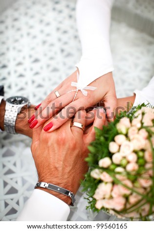 Groom and bride are holding hand of each other with feelings of love. Luxury decoration like a bouquet from roses, golden wedding rings and beautiful manicure.