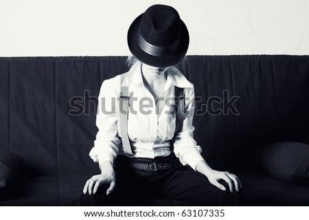 Woman in classic men's hat, and a shirt sitting on the sofa