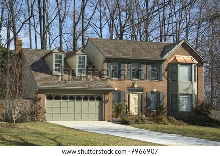 Large suburban colonial-style brick house with green shutters, bay windows and copper trim