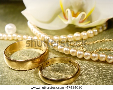 stock photo Gold wedding rings with pearls on green satin with orchid