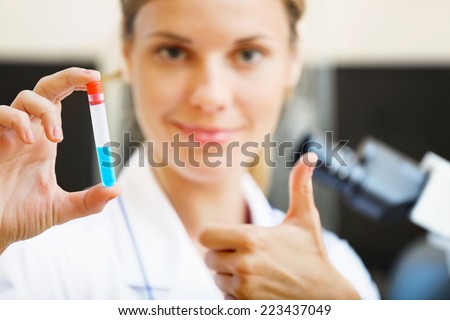 Happy young beautiful scientist holding samples with positive testing results in her hand.