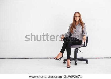 Portrait of young beautiful business woman sitting on chair against white wall.