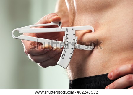 Young man is measuring his body fat with calipers.