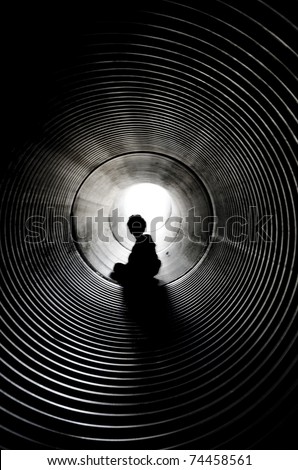 The silhouette of the sitting boy with light at the end of tunnel