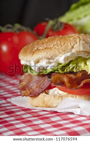 Bacon, lettuce and tomato sandwich or BLT freshly made, with vibrant, healthy colours on a red gingham tablecloth with whole tomatoes and lettuce in the background