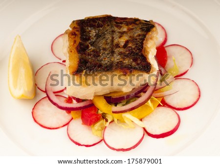 Seared cod fillet with crispy brown skin and accompanied by a salad of red onion, yellow pepper and radish slice, dressed with olive oil and lemon. n a white plate.