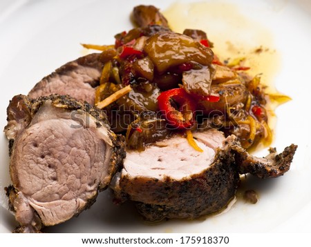 Roast fillet of pork marinaded in dried mint, olive oil and orange zest.  Caramelised garlic and orange skin with orange juice, olive oil and red chili.  On a white plate.