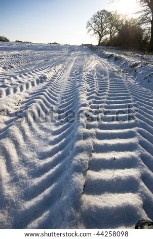 Deep tractor tracks in the snow at the edge of a ploughed field.