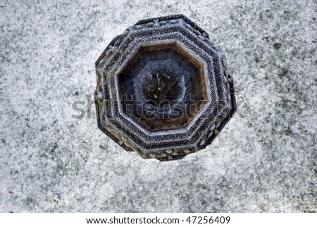 Frozen birdbath from directly above, covered in ice crystals, on a snow covered lawn