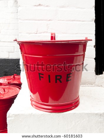 Striking retro red fire bucket on a white doorstep against a white painted brick wall.