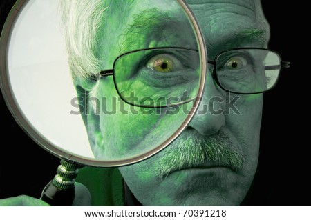 Green face of a man with yellow eyes and  glasses looking through a magnifying glass with a grim expression on his face. On black.
