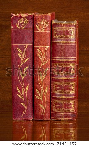 Three antique red leather bound  books standing up on a polished wooden shelf.