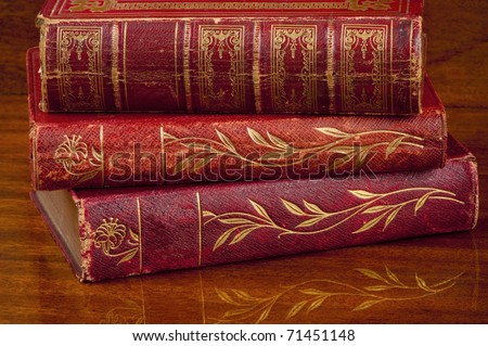 Three decorated antique red leather bound  books stacked on a polished wooden shelf.