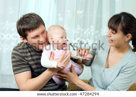 happy family home: father, mother and baby sitting against the window