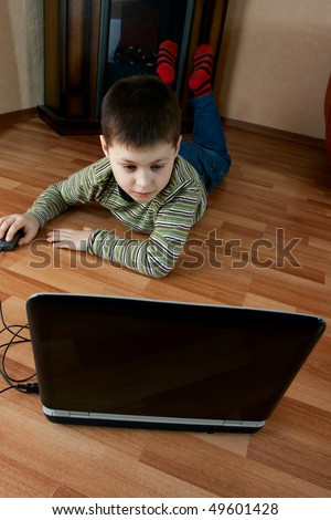 little boy lying down on the floor in the living room and playing computer game on laptop