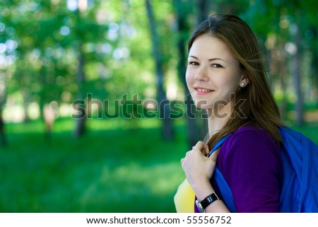 young female student with backpack walking in the park
