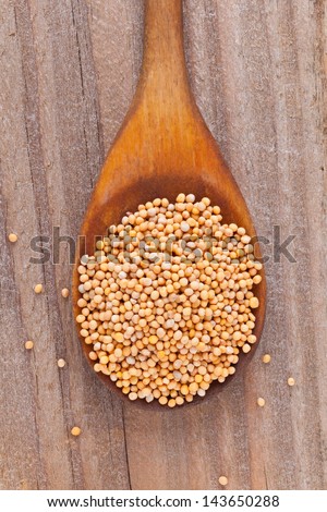 Mustard seeds on wooden spoon on rustic kitchen table