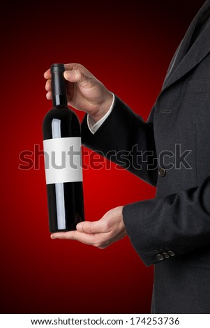 Man in suit holding red wine bottle isolated on red background