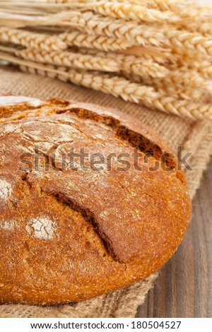 Whole loaf of fresh bread with wheat ears on burlap on wooden table