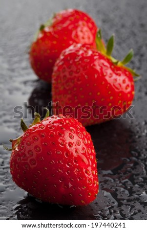 Three ripe whole organic strawberries on black cutting board with water drops