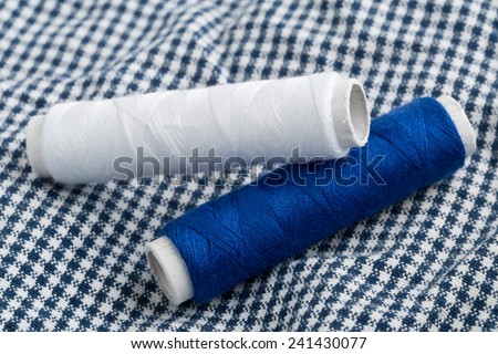 Blue and white sewing yarn roll on white and blue textile fabric background