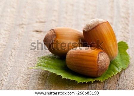 Heap of organic hazelnuts on hazelnut leaf over wood background - selective focus macro shot