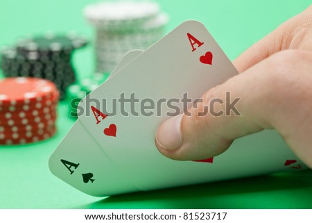 Pokerplayer shows pocket aces with poker chips in the back over green background