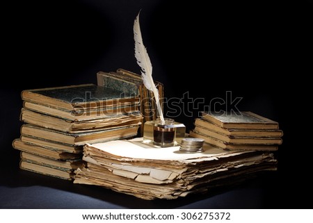 Old fountain pen, books and inkwell and silver coins on a black textured background