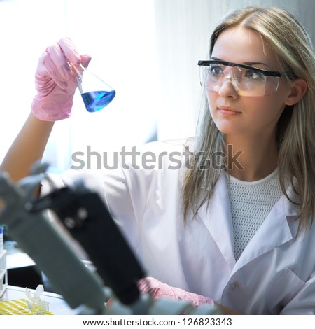 female researcher look at retort with blue liquid