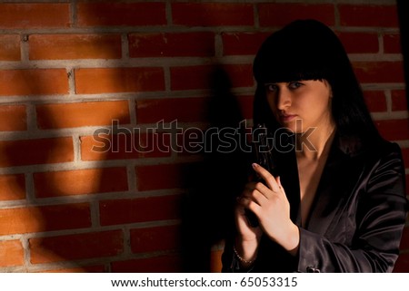 Young woman with hand gun near brick wall