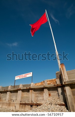 beach safety warning sign and flag against a clear blue sky