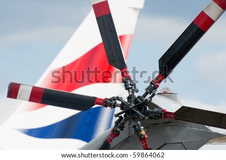 helicopter rotor blades with a large jet aircraft tail fin in the background