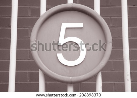 Number Five on Circle against Brick Wall and Railings Background in Black and White Sepia Tone