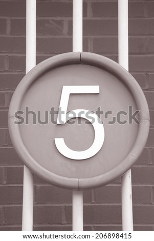 Number Five on Circle against Brick Wall and Railings Background in Black and White Sepia Tone
