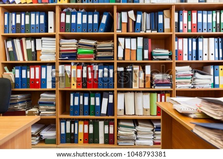 Wall from shelves with colourful file binders, interior of an office room with papers and documents