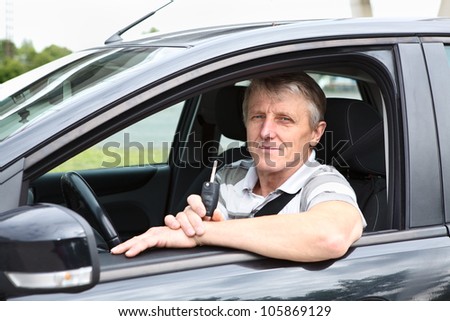Happy senior male with ignition key sitting in car on driver seat and smiling
