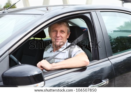 Fastened smiling Caucasian senior man sitting in car on driver seat