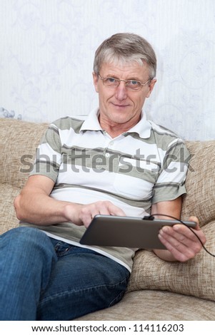 Senior adult Caucasian man working with a new tablet computer, sitting on sofa in domestic room