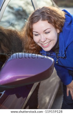 Smiling woman admire oneself in car rear-view side mirror against sunlights