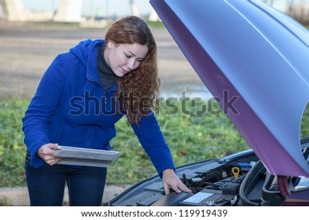 Woman a driver with touchpad repairing broken car with opened engine hood