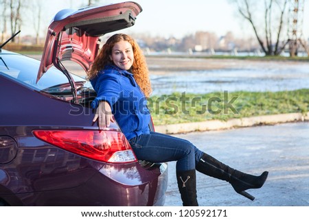 Young woman in boots sitting in car luggage trunk