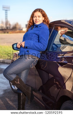 Serene woman with curly hair leaning to car in sunbeams