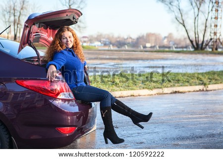 Joyous young woman sitting in car luggage trunk