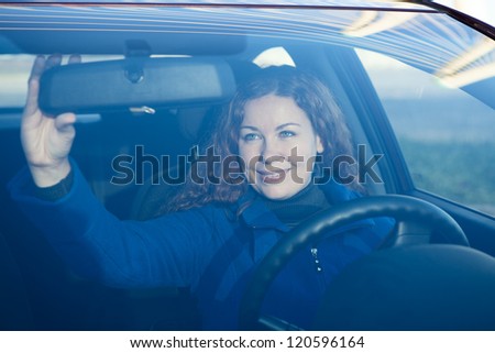 Pretty woman in car preparing to driving correcting back mirror
