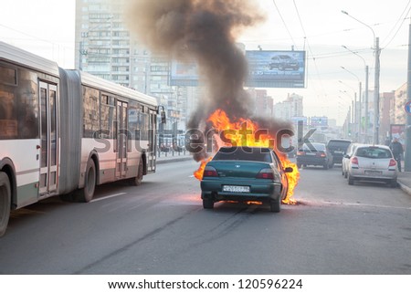 SAINT-PETERSBURG, RUSSIA-NOVEMBER 11: Passenger transport passes near burning car on city street on November 11, 2012 in Saint-Petersburg, Russia. Self-ignition car wiring. No one was injured.