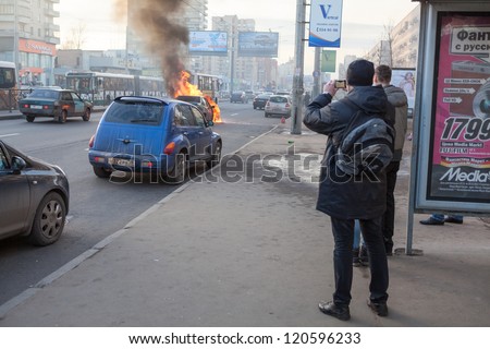 SAINT-PETERSBURG, RUSSIA-NOVEMBER 11: Passers-by shoot video with a burning car on the urban road on November 11, 2012 in Saint-Petersburg, Russia. Self-ignition car wiring. No one was injured.