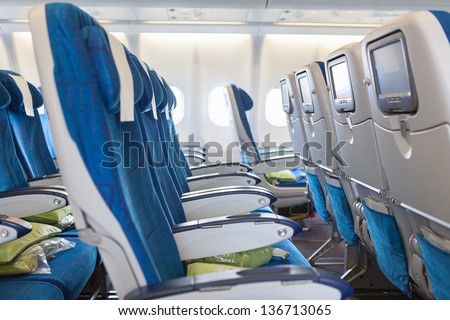 Empty comfortable seats in cabin of huge aircraft with screens in chairs back