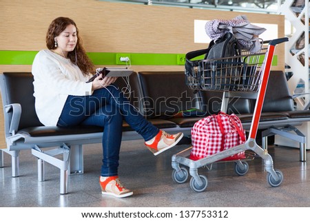Woman looking at tablet pc in airport lounge with luggage hand-cart