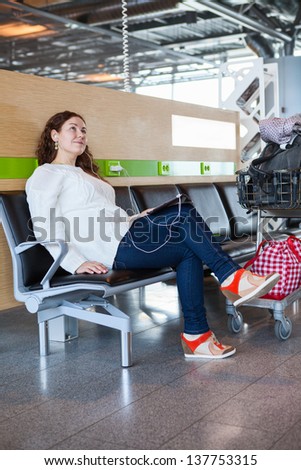 Woman dreaming with tablet pc in airport lounge with luggage hand-cart