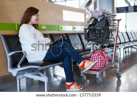 Woman spending time with tablet pc in airport lounge with luggage hand-cart